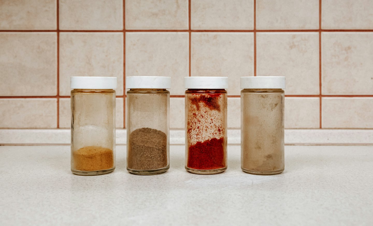 Four glass spice jars on a kitchen counter.