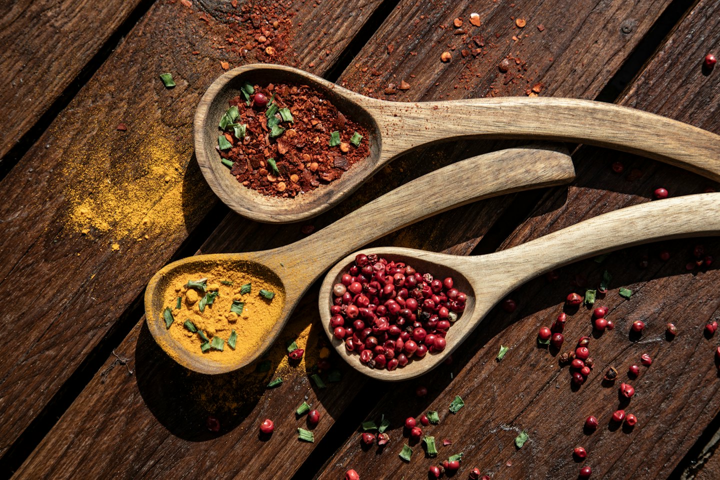 Wooden spoons with chili, turmeric, and peppercorns on a table.