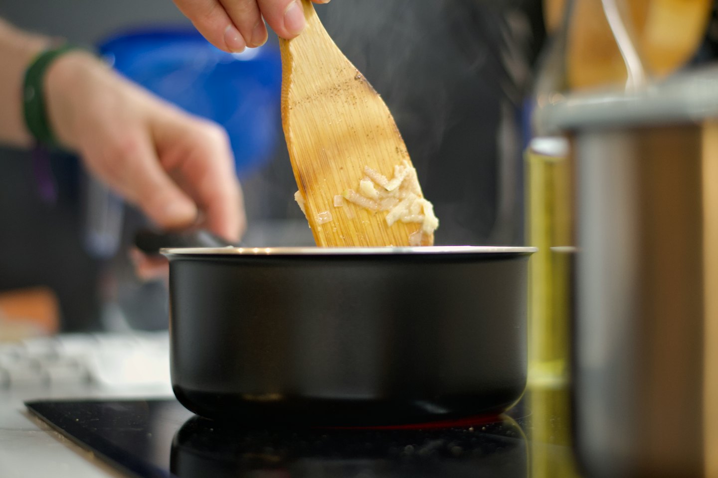 Hands stir chopped vegetables in a saucepan with a spoon.