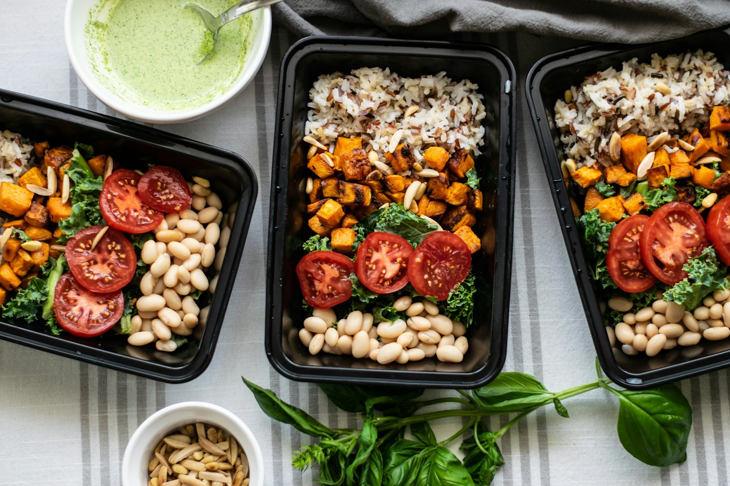 Three meal prep containers filled with healthy food on a striped tablecloth.