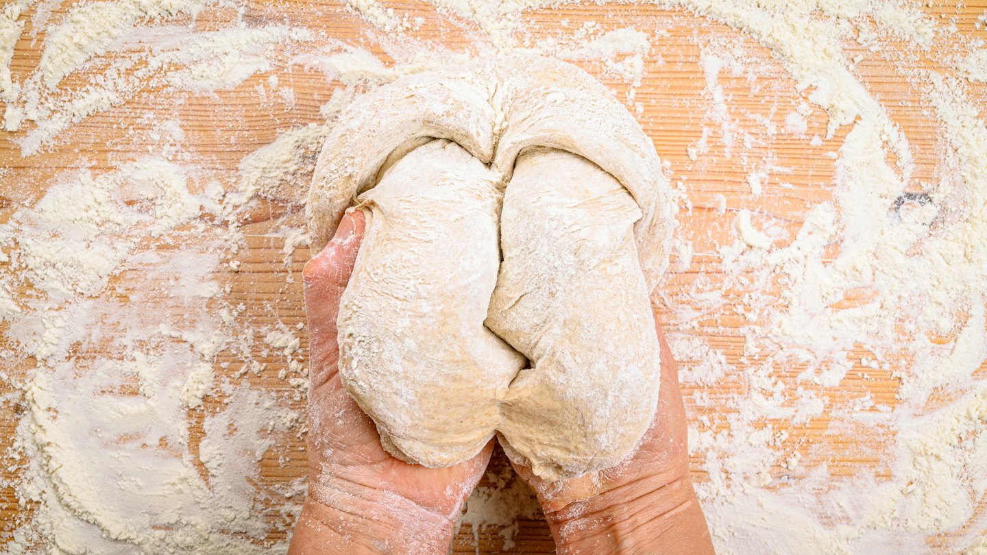 Hands kneading dough on a floured wooden kitchen counter.