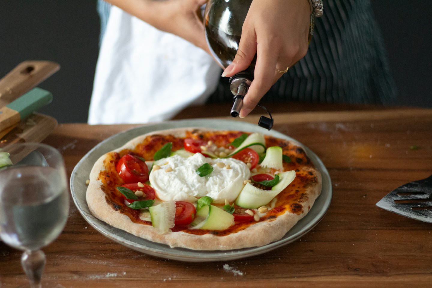Hands drizzle olive oil over a fresh burrata pizza.