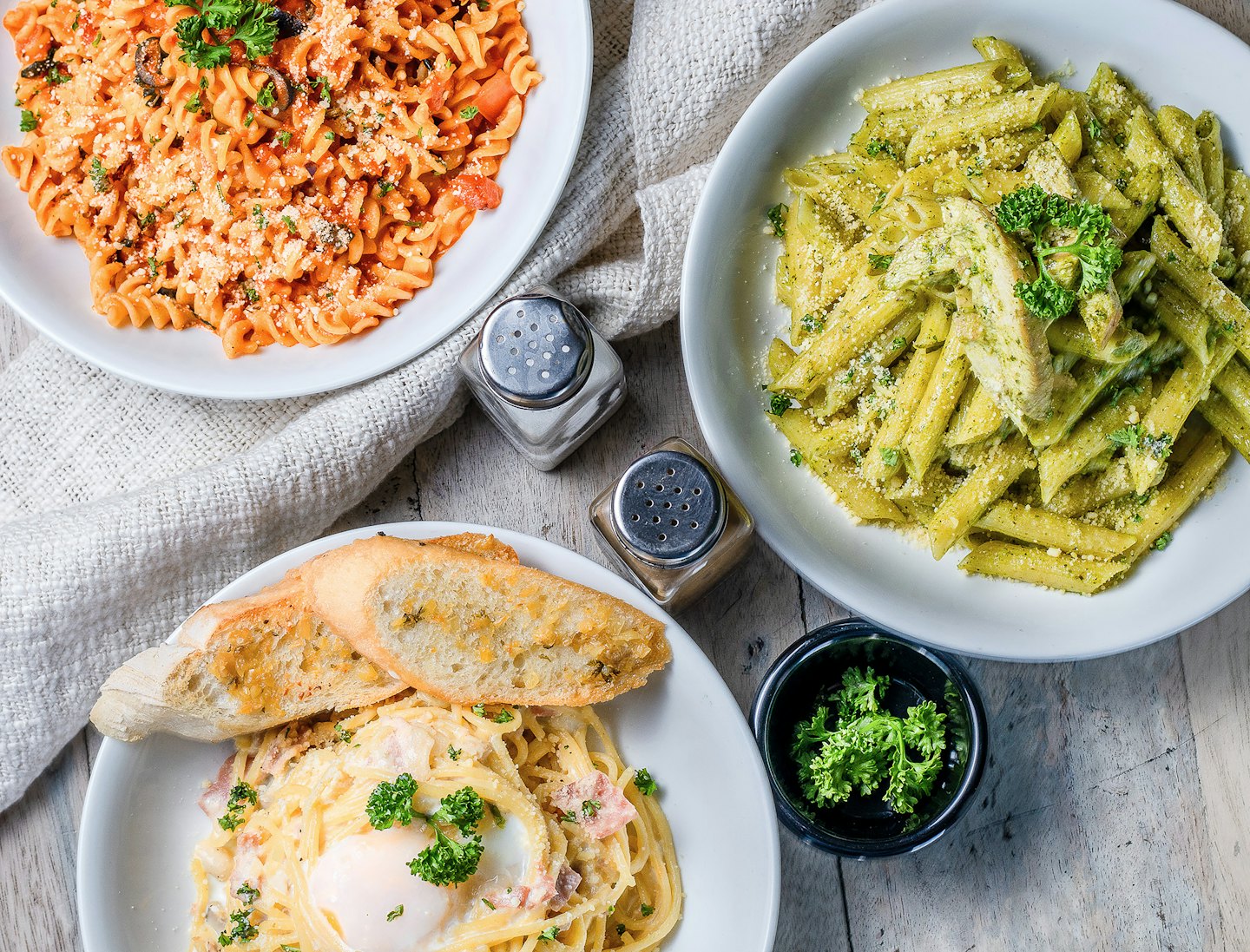 Three distinct pasta dishes arranged on a wooden table.