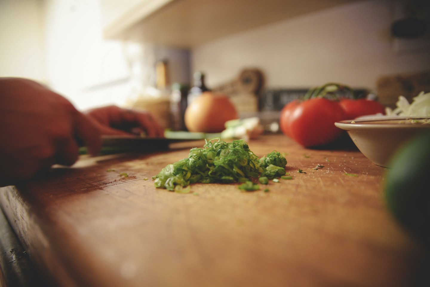 Hands chopping green onions on a wooden cutting board.