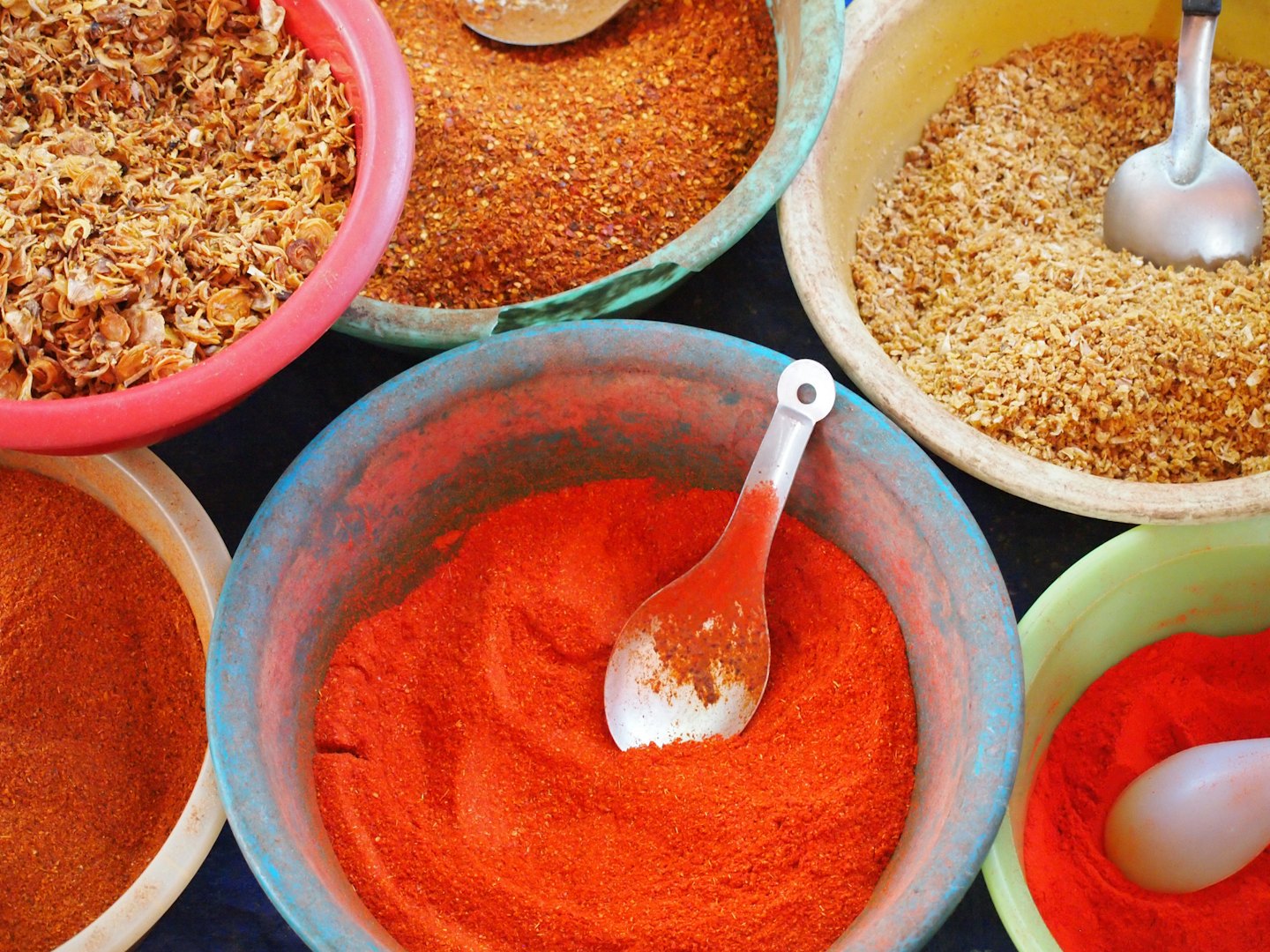 Colorful spice bowls with tasting spoons and various dried ingredients.