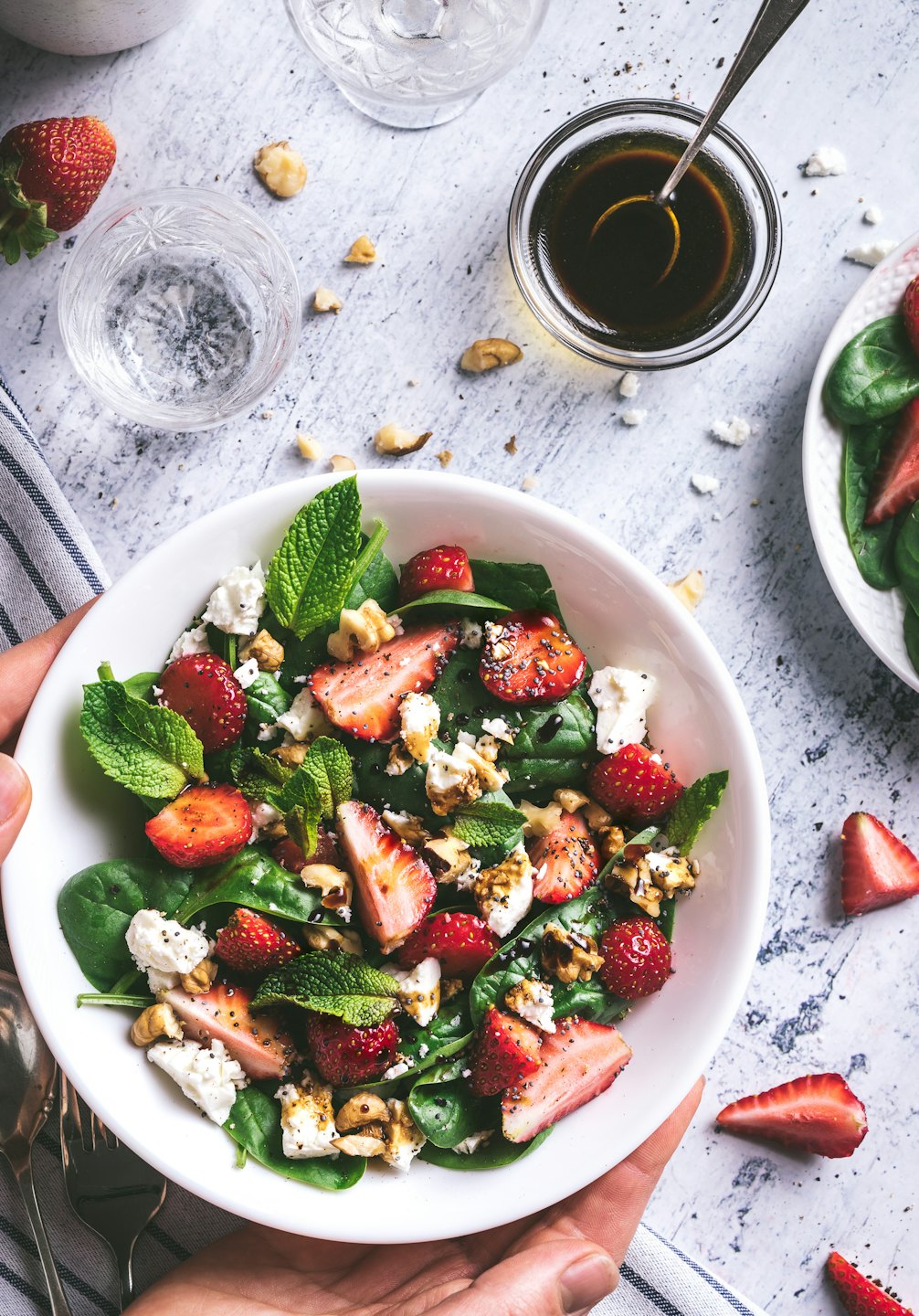 Hands holding a bowl of vibrant spinach strawberry salad.