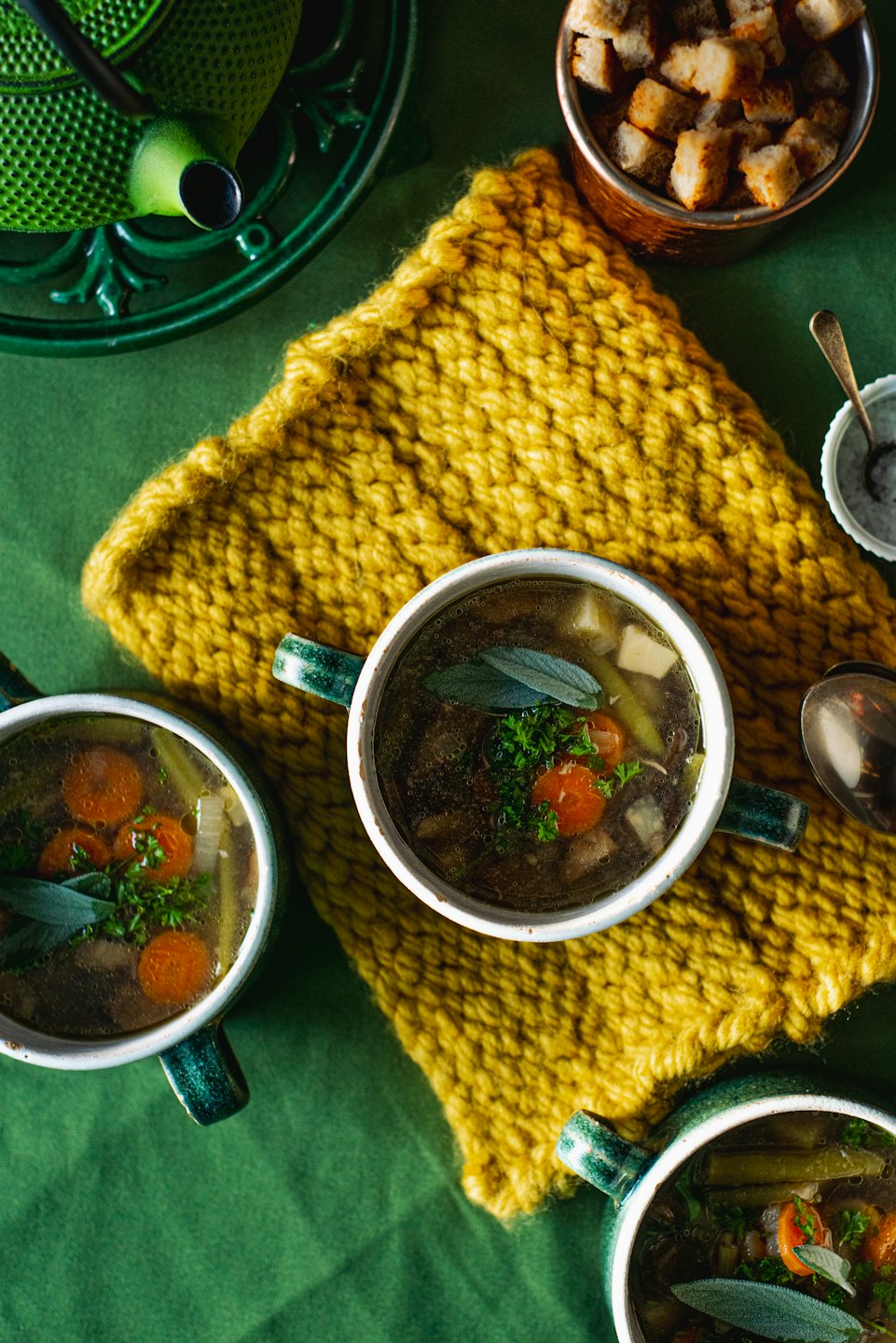Three bowls of hearty soup with fresh herbs on a green tablecloth.